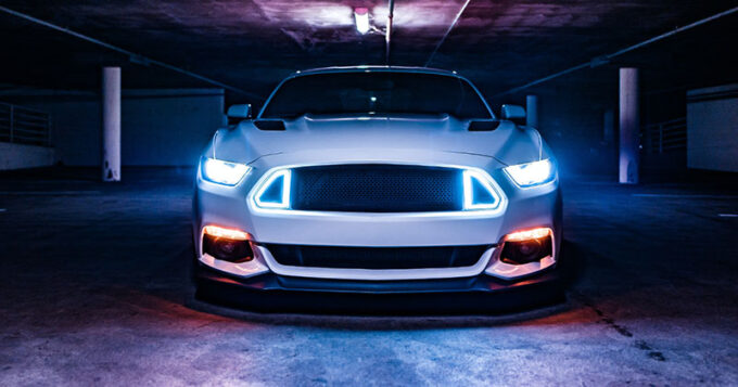 A mustang in a garage with its headlights on