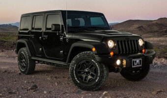 A black jeep wrangler in the desert at dusk with it's headlights on